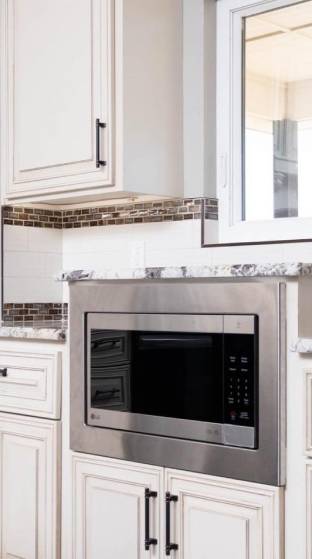 Front view of kitchen with white wood and metallic color microwave